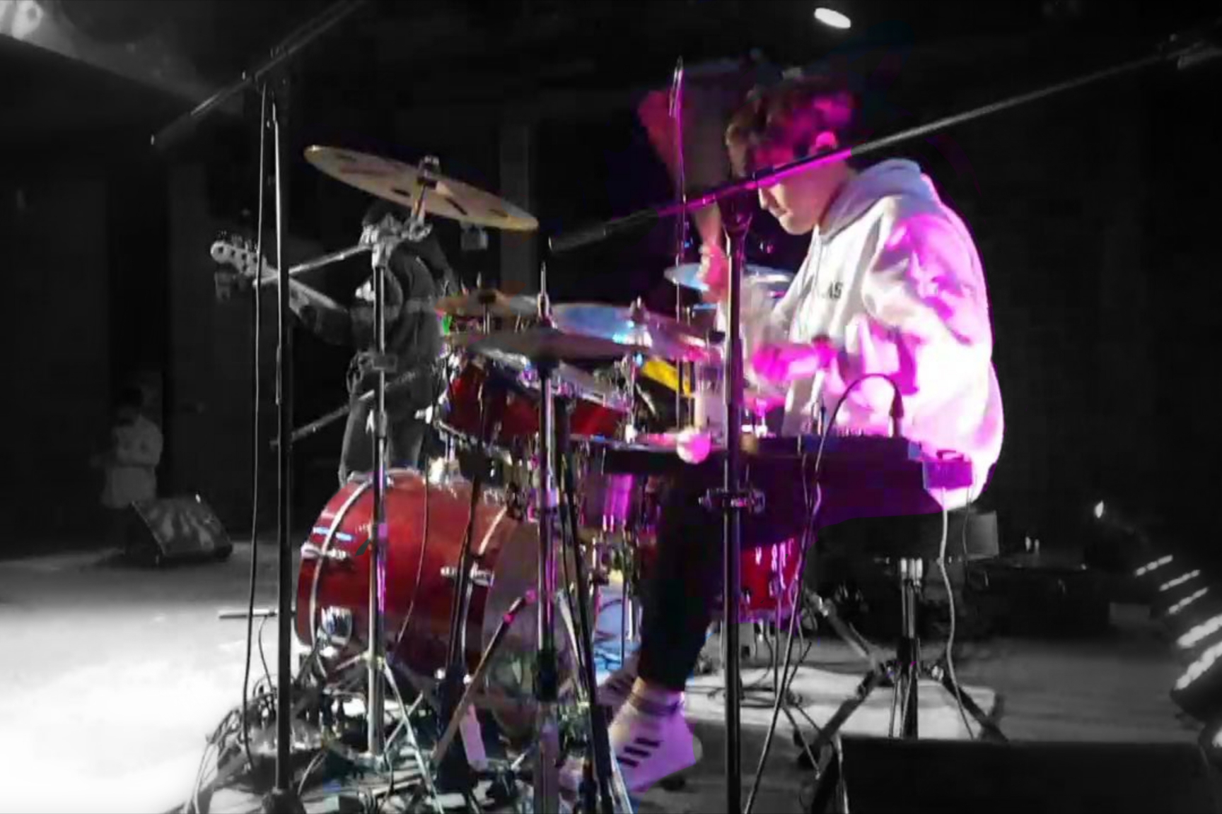 Sungjoon Kim playing a red acoustic drum kit under purple stage lighting
