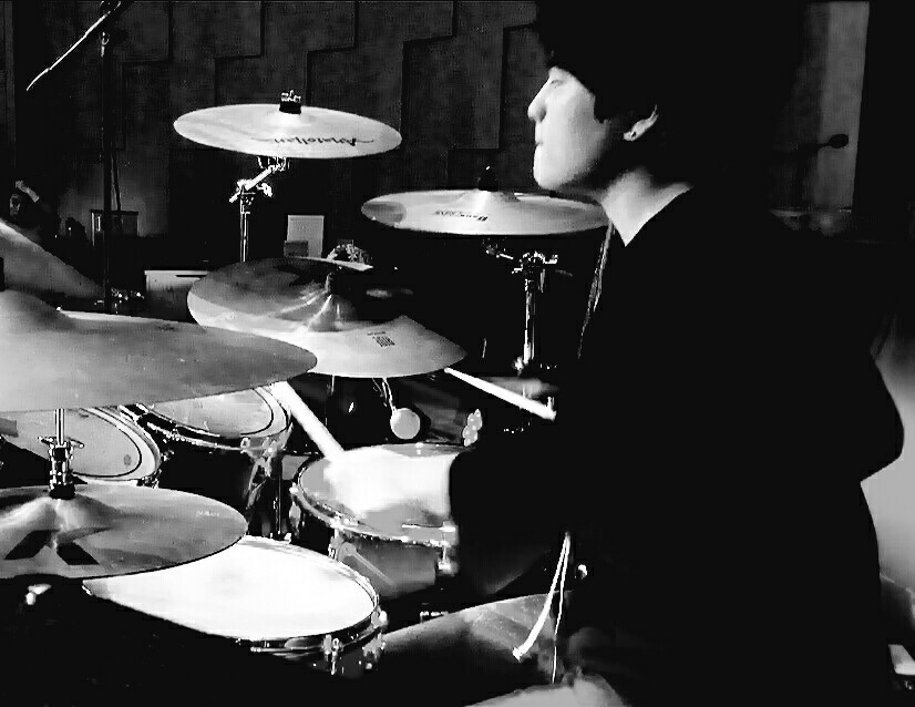 Black-and-white photograph of Sungjoon Kim playing an acoustic drum kit