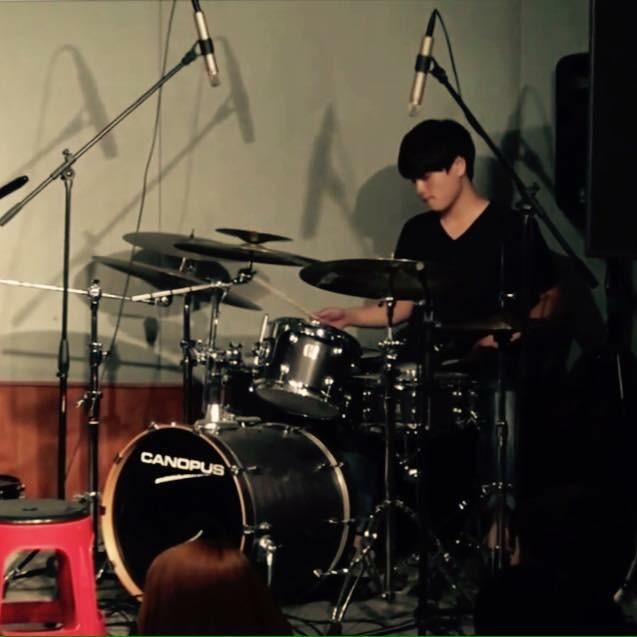Sungjoon Kim performing on a black acoustic drum kit with overhead microphones